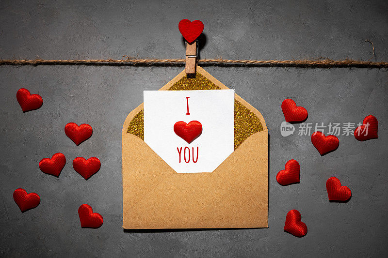 clothespins with red hearts on a rope on a gray background. postcard with text i love you on paper